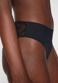 Svart bikiniunderdel i ribbat material, med en spetspanel på sidan. Slät textur med en måttlig hög midja.