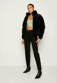 Černá sametová bomber bunda s cropped designem, zelený pletený top, černé džíny s vysokým pasem a černé kotníkové boty, zvoucí se elegantním siluetou.