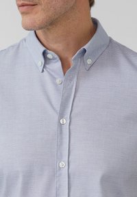 Lichtblauw button-up overhemd met een getextureerd visgraatpatroon, voorzien van een button-down kraag en witte knopen.