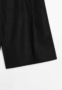 Pantaloni corti neri sartoriali realizzati in un tessuto leggero con una sottile trama. Presentano gambe larghe e una finitura pulita lungo l'orlo.