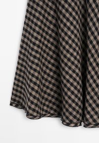 Tissu fluide avec un motif à carreaux noir et beige formant des lignes diagonales et des plis doux.