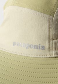 Κοντινή λήψη ενός καπέλου τύπου bucket της Patagonia σε μπεζ και ανοιχτό πράσινο χρώμα, που δείχνει ραμμένα πάνελ και λεπτομέρειες στη γυριστή γείσο.