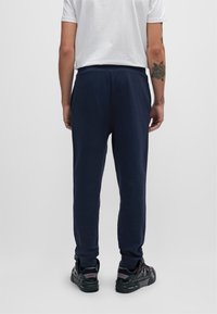 Marineblaue Jogginghosen mit einem Kordelzugbund, Seitentaschen und elastischen Bündchen, kombiniert mit schwarzen Sneakers mit roten Akzenten.