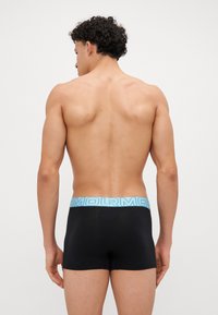 Sorte boxer briefs med en lyseblå logo-linning, med et tætsiddende design og glat stoftekstur, set fra bagenden.