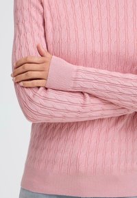 Maglione rosa chiaro con motivo a treccia testurizzata, polsini e orlo a costine. Materiale morbido, stile aderente, presenta maniche lunghe con finiture curate.