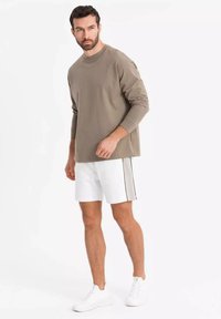 Chemise olive à manches longues, shorts blancs avec une bande latérale noire, et baskets blanches. Le tissu semble lisse et décontracté dans son design.