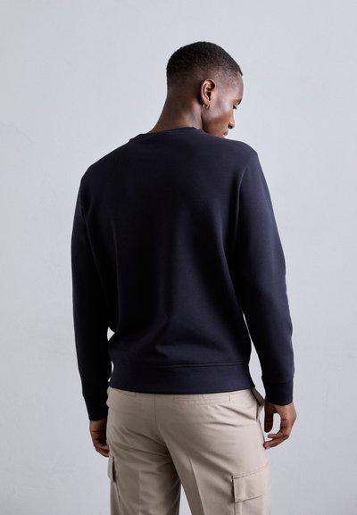 Sötétkék pulóver hosszú ujjakkal és kerek nyakkivágással, puha anyagból készült. Látványos bordás mandzsettákkal és aljjal, bézs cargo nadrággal párosítva.