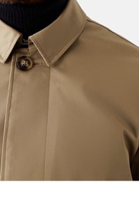 Beige Regenmantel mit klassischem Kragen und einem einzigen Knopfverschluss. Der glatte Stoff hat ein mattes Finish. Keine sichtbaren Muster oder Verzierungen.