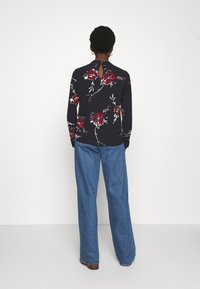 Maglia nera a maniche lunghe con motivo floreale rosso, dotata di apertura a chiave sul retro. Abbinata a jeans in denim blu a gamba larga. Design semplice e vestibilità comoda.