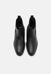 Black leather chelsea boots featuring a smooth texture, elastic side panels, and pull tabs for easy wear. Sole has a slight tread.