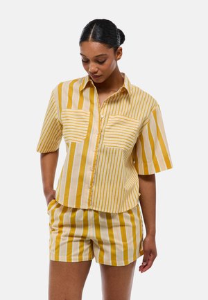 Ensemble composé d'une chemise à manches courtes rayée et d'un short en jaune et blanc. Comprend des boutons, deux poches devant et une coupe décontractée. Matériau en coton.