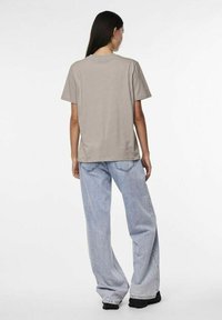 Gaiši pelēka īsām piedurknēm t-kreklā ar brīvu piegriezumu, apvienots ar gaiši ziliem vaļīgiem džinsiem; attēlots no aizmugures.