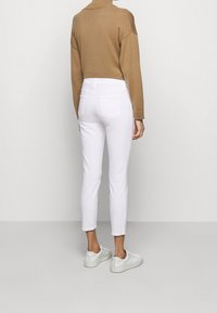 Jeans blancos ajustados con bolsillos traseros, combinados con un suéter de punto marrón y zapatillas blancas. Tejido suave y corte entallado.