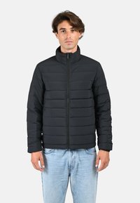 Veste matelassée noire avec col montant, dotée d'une fermeture éclair à l'avant, d'un design à soufflets horizontaux et d'une texture lisse et brillante.
