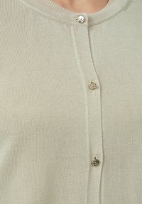 Hellbeige Strickjacke mit geripptem Muster, Rundhalsausschnitt und drei Knöpfen an der Vorderseite. Weiches Material mit einem schlichten Design.