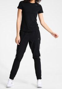 Black short-sleeve t-shirt and matching joggers with white side stripes. Made of lightweight fabric, featuring an athletic fit and elastic cuffs.