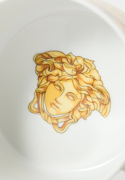 Λευκό κεραμικό μπολ με μια περίπλοκη κίτρινη και πορτοκαλί απεικόνιση ενός προσώπου με σγουρά μαλλιά, στο κέντρο του μπολ.