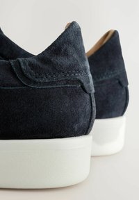 Paire de chaussures slip-on en daim bleu marine foncé avec semelles épaisses en caoutchouc blanc, vue de dos.