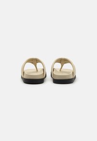 Beige sandaler med en glat overflade, der har et minimalistisk design, flad sort sål og minimale stropper for nem påføring.