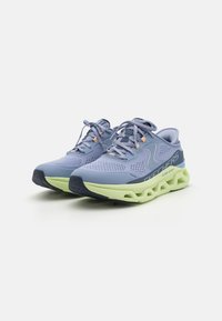 Baskets de sport bleu clair avec une tige en mesh, des accents texturés et une semelle intermédiaire en mousse verte avec un design découpé distinctif.