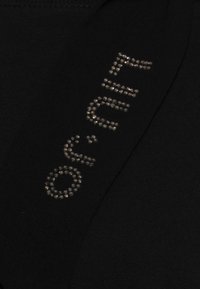 Svart tyg med en metallisk nitar-design där bokstäverna "of" framhävs med böjda rhinestone-accenter.