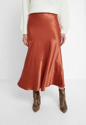 Jupe midi en satin, couleur orange rouille, avec une texture lisse et un design fluide. Associée à des bottines à motifs.