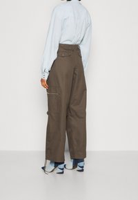 Brązowe spodnie cargo z wysokim stanem, kieszeniami bocznymi i luźnym krojem, w połączeniu z jasnoniebieską koszulą na guziki oraz wzorzystymi niebieskimi skarpetkami.