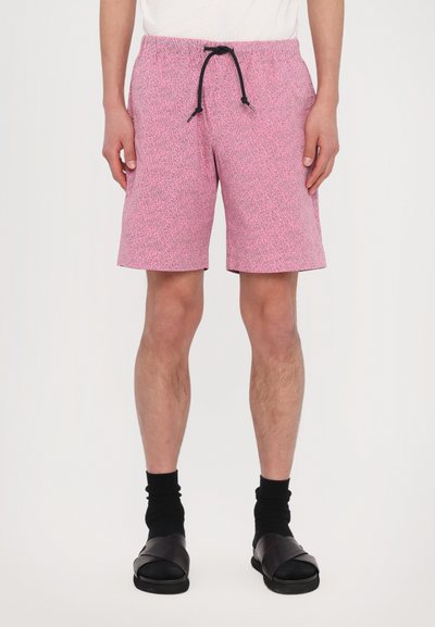 Rosa Badeshorts mit strukturiertem Muster, elastischem Bund und schwarzem Kordelzug. Getragen mit schwarzen Socken und schwarzen Sandalen.