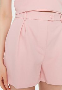 Helle rosa maßgeschneiderte Shorts aus glattem Stoff, mit Gürtelschlaufen, einem Frontknopfverschluss und dezenten Falten für zusätzlichen Detailreichtum.