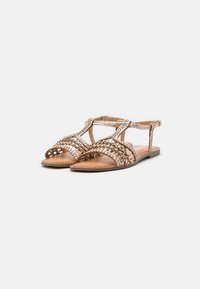Sandalias de cuero trenzado con un tono bronce, diseño de puntera abierta y tira para el tobillo; suela plana y detalles trenzados en la parte superior.