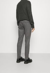 Pantalons gris à motifs avec une coupe slim, dotés d'une poche arrière boutonnée, associés à un pull en texture sombre et des chaussures noires.