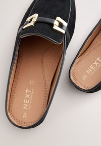 Mocassins en daim noir avec un accent de boucle dorée, semelle intérieure lisse marron étiquetée "NEXT Forever Comfort". Bout arrondi et semelle plate.