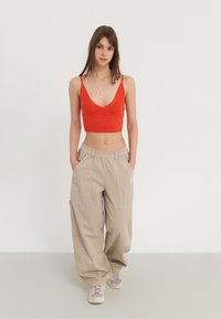 Rød strikket crop top med V-hals og åpen vev, kombinert med vide beige cargo-bukser med lommer og snøring. Lette grå sneakers.