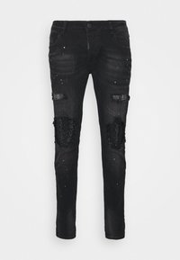 Jeans de mezclilla negra con parches desgastados, adornados con detalles de cuentas y un diseño ajustado. Costuras visibles y cierre de botón.