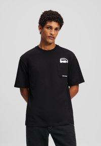 Zwarte korte mouw t-shirt gemaakt van katoen. Heeft een borstzak met een wit logo en een relaxte pasvorm. Gladde textuur.