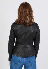 Svart läderjacka med strukturerade sömmar och peplummidja, med långa ärmar och en slät textur, bärs över blå denimjeans.