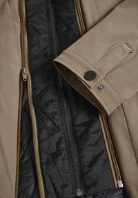 Chaqueta exterior color beige con forro negro, que presenta cierres dobles, puños abotonados y una textura suave.