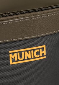 Bolsa de tela negra con una superficie texturizada, que presenta un acento de cuero marrón y un logo amarillo de "MUNICH" en la parte frontal. Cierre con cremallera.