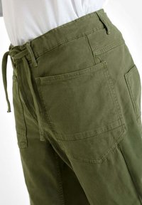Witte shirt in een olijfgroene broek gestoken met grote achter- en zijzakken en een knoopceintuur.