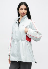 Helehall hall jope punaste detailidega ja elastse vöökohaga, millel on kõrge krae, tõmblukk ja lahtised varrukad. Nike logo rinnal.