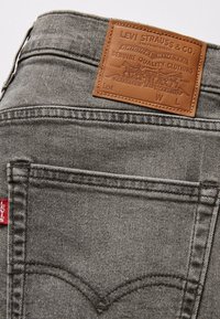 Poche arrière en jean gris Levi's avec étiquette rouge Levi's et étiquette de marque en cuir marron cousue sur la ceinture.
