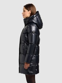 Tmavomodrý vatovaný kabát s lesklým povrchom, kapucňou a vreckami na zips. Má prešívaný dizajn a logo na rukáve. Nastaviteľný strih.