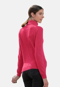 Pull en tricot rose avec un col montant, présentant un motif en losanges texturé, une coupe ajustée et des manches longues. Associé à un jean foncé.