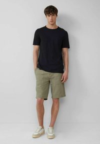 Black short-sleeve t-shirt with a chest pocket, paired with light olive green shorts featuring side pockets and beige sneakers with white laces.
