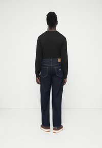 Μαύρο μακρυμάνικο πουκάμισο, μπλε τζιν από denim, σκουρόχρωμο πλύσιμο, κανονική εφαρμογή με ίσια μπατζάκια, δερμάτινο ταμπελάκι στη μέση, καφέ αθλητικά παπούτσια με λευκή σόλα.