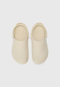 Sabots beige avec une texture lisse, un bout rond et une sangle au talon. Comprend un logo subtil sur le côté et un design de semelle intérieure contour.