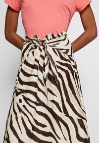Zebra-striped skirt in beige and brown fabric, featuring a tied waist and a ruffled top edge. Material appears lightweight and textured.