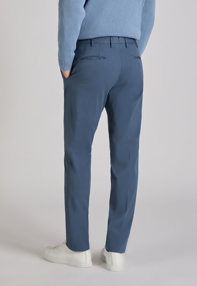 Blaue Hose aus glattem Stoff, mit schmaler Passform, zwei Gesäßtaschen und einem Bund mit Gürtelschlaufen, kombiniert mit weißen Turnschuhen.