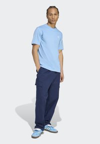 Light blue cotton t-shirt with short sleeves and white logo, paired with navy cargo pants featuring side pockets and blue sneakers with white details.