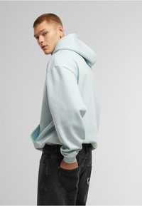 Felpa con cappuccio di colore azzurro chiaro, dal fit rilassato, con cordoncino e tasca a marsupio, abbinata a jeans grigio scuro con dettagli sulle tasche.